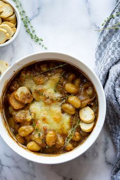 a bowl of french onion gnocchini soup on a marble table with crackers