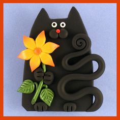 a black cat holding a yellow flower on top of it's back with green leaves