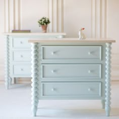 a white dresser sitting next to a table with a vase on it's top