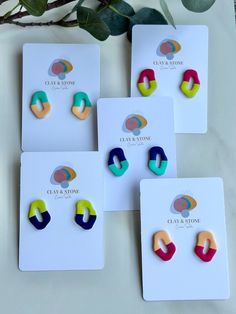 four pairs of colorful earrings sitting on top of a white card next to a plant