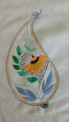 an embroidered piece of cloth with flowers and leaves on the side, sitting on top of a tablecloth