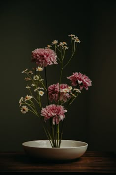 pink and white flowers are in a bowl on a wooden table with dark walls behind them