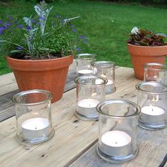 a table topped with lots of glass vases filled with candles next to potted plants