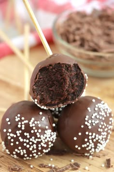 three chocolate covered donuts with sprinkles on a wooden board next to a bowl of brownie holes