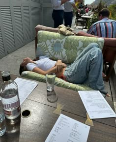 a woman laying on top of a couch next to a table filled with papers and drinks