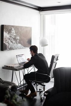 a man sitting at a desk with a laptop computer in front of him and looking out the window