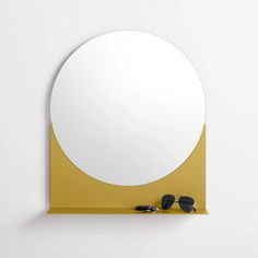 a round mirror mounted on the wall above a pair of sunglasses and a yellow shelf