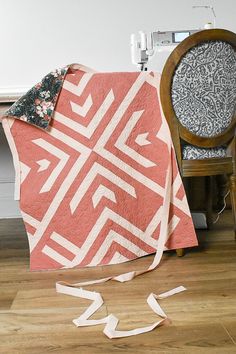 an orange and white quilt sitting on top of a wooden floor next to a chair