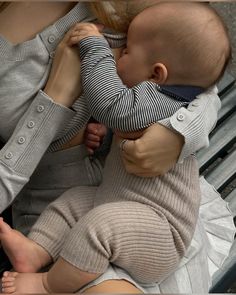 a woman holding a baby in her arms on top of a park bench with the child's arm wrapped around him