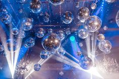 many shiny balls hanging from the ceiling in front of bright blue lights and spotlights