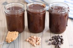 three jars filled with peanut butter, chocolate and cashews on top of a wooden table