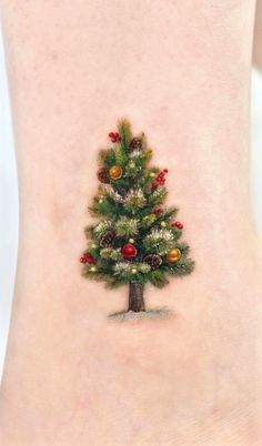 a small christmas tree tattoo on the side of a woman's leg, with ornaments around it