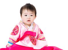 a baby sitting on the ground wearing a pink outfit and holding a red object in its hand