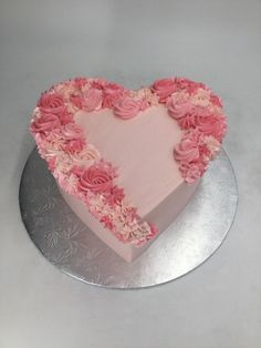 a heart shaped cake with pink frosting and roses on it's side, sitting on a silver platter