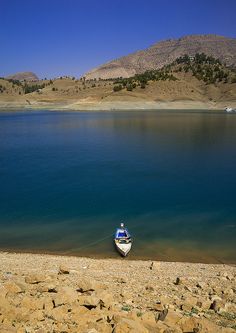 a small boat sitting on top of a lake next to a rocky shore with mountains in the background