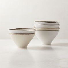 four white bowls stacked on top of each other in front of a white wall and floor