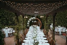 an outdoor dining area with white tablecloths and lights strung over the top of it