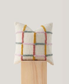 a white and yellow pillow sitting on top of a wooden stand next to a wall