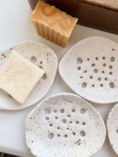 four white ceramic plates with holes on them next to a wax block and soap dish