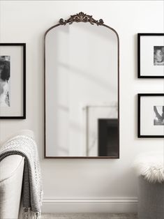 a mirror sitting on top of a white wall next to a chair and pictures hanging on the wall