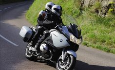 two people riding on the back of a silver motorcycle down a curvy road