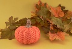 a crocheted pumpkin sitting next to some leaves