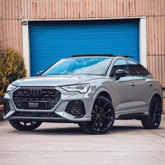 a silver audi suv parked in front of a garage door with blue roller shutters