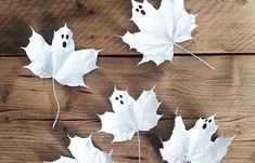 four white leaves with ghost faces on them are hanging from the side of a wooden wall