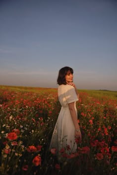 a woman standing in a field full of red and white flowers with her hand on her chin