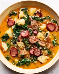 a bowl filled with sausage, potatoes and spinach on top of a white table