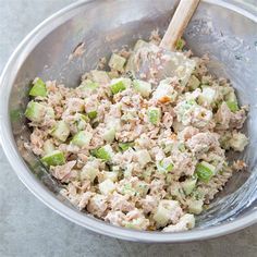 a bowl filled with tuna and celery on top of a table next to a wooden spoon