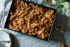 a pan filled with pasta and sauce on top of a table next to some flowers