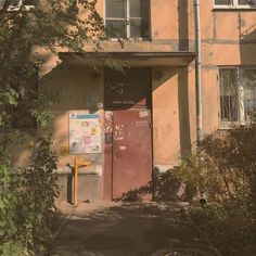 an old building with a red door and sign on the side walk next to it