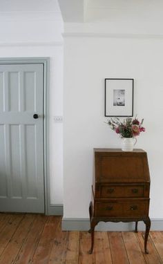 a room with white walls and wooden flooring has a plant on top of the dresser