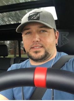 a man sitting behind the wheel of a car wearing a hat and holding a steering wheel