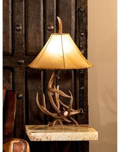 an antler lamp on a table next to a brown chair and wooden wall with doors