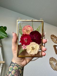 a person holding up a small glass box with flowers in it on the wall behind them