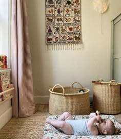 a baby laying on its back in a room with two baskets and a wall hanging