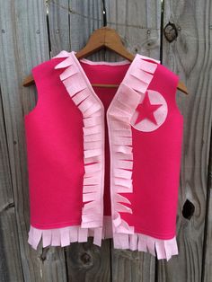 a pink vest with ruffles and a star on it hanging on a wooden fence