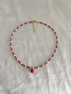 a red and white beaded necklace with a cross on the end, sitting on a white sheet