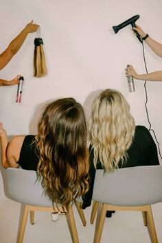 two women sitting in chairs with hair dryers on the wall behind them and blowdrying their hair