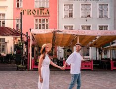 a man and woman holding hands in front of some colorful buildings on a cobblestone street