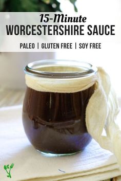 a jar filled with brown sauce sitting on top of a white cloth next to a potted plant