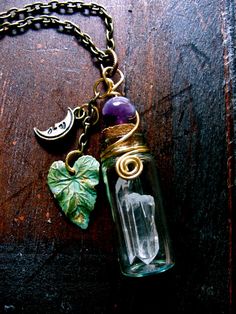 a necklace with a glass bottle and charms attached to it on a wooden table next to a chain