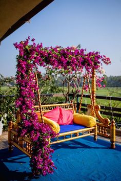 an outdoor swing bed with purple flowers on it and blue carpeted area in the foreground