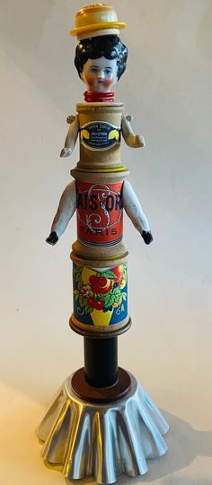 a small doll sitting on top of a stack of tin canisters with other items around it