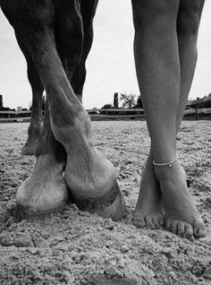 a black and white photo of a person standing next to a horse with their feet on the ground