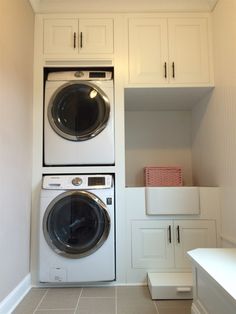 a washer and dryer in a white laundry room with cabinets on either side