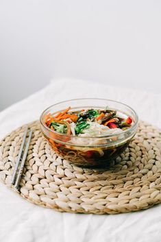 a bowl of food sitting on top of a woven place mat next to a fork