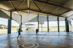 three people playing basketball in an indoor court with the sun shining on them and one person holding a blue frisbee